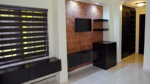 Uma sala de estar moderna com uma televisão de tela plana montada em uma parede de tijolos, um rack de entretenimento preto e uma janela com persianas.