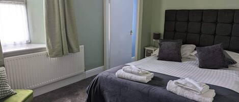 Une chambre bien rangée, avec un lit, une chaise, une table de chevet et une fenêtre avec des rideaux.