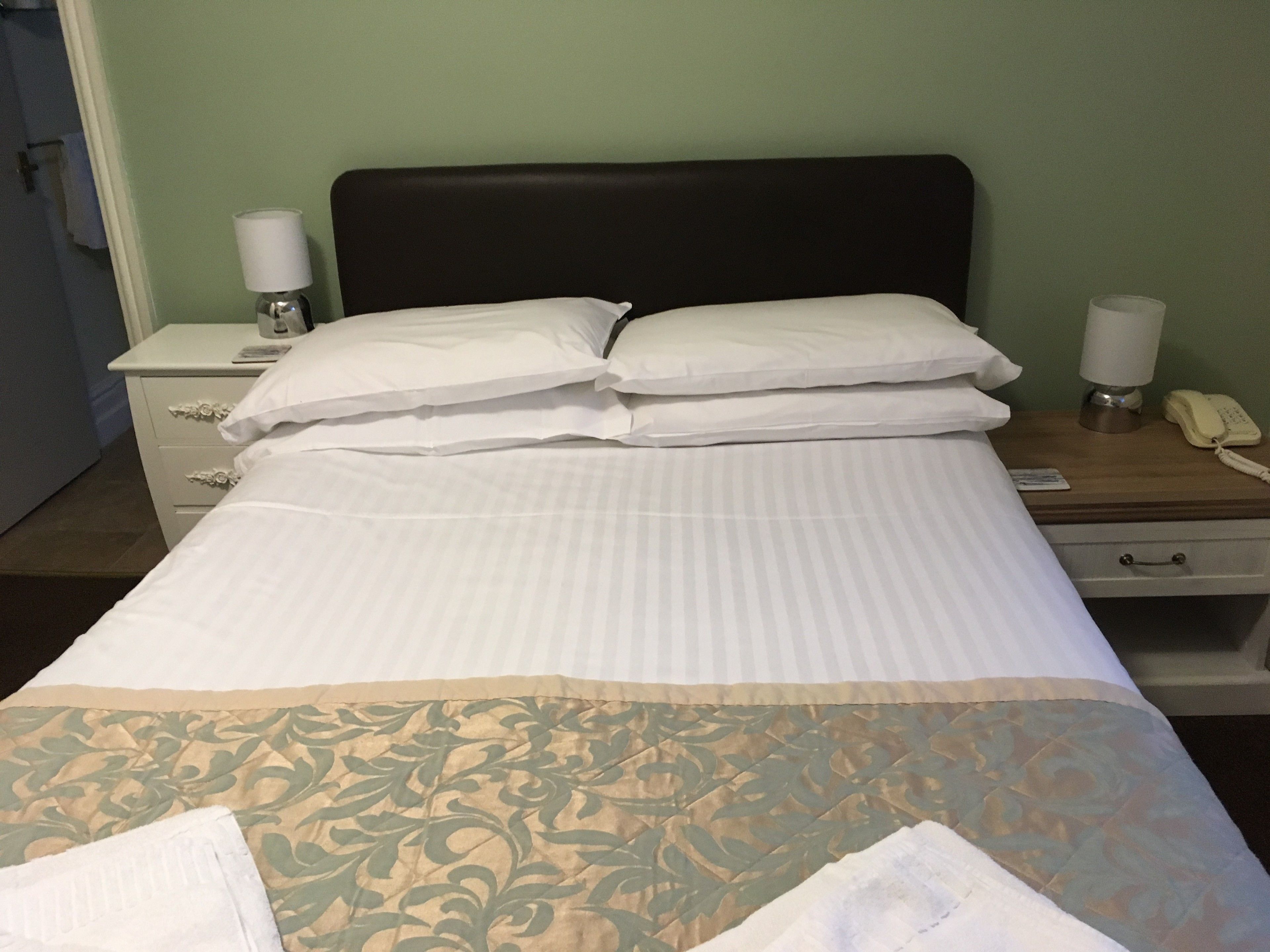 Ein ordentlich bezogenes Bett mit weißen Bettwäsche, einer gemusterten Tagesdecke und zwei Nachttischlampen.