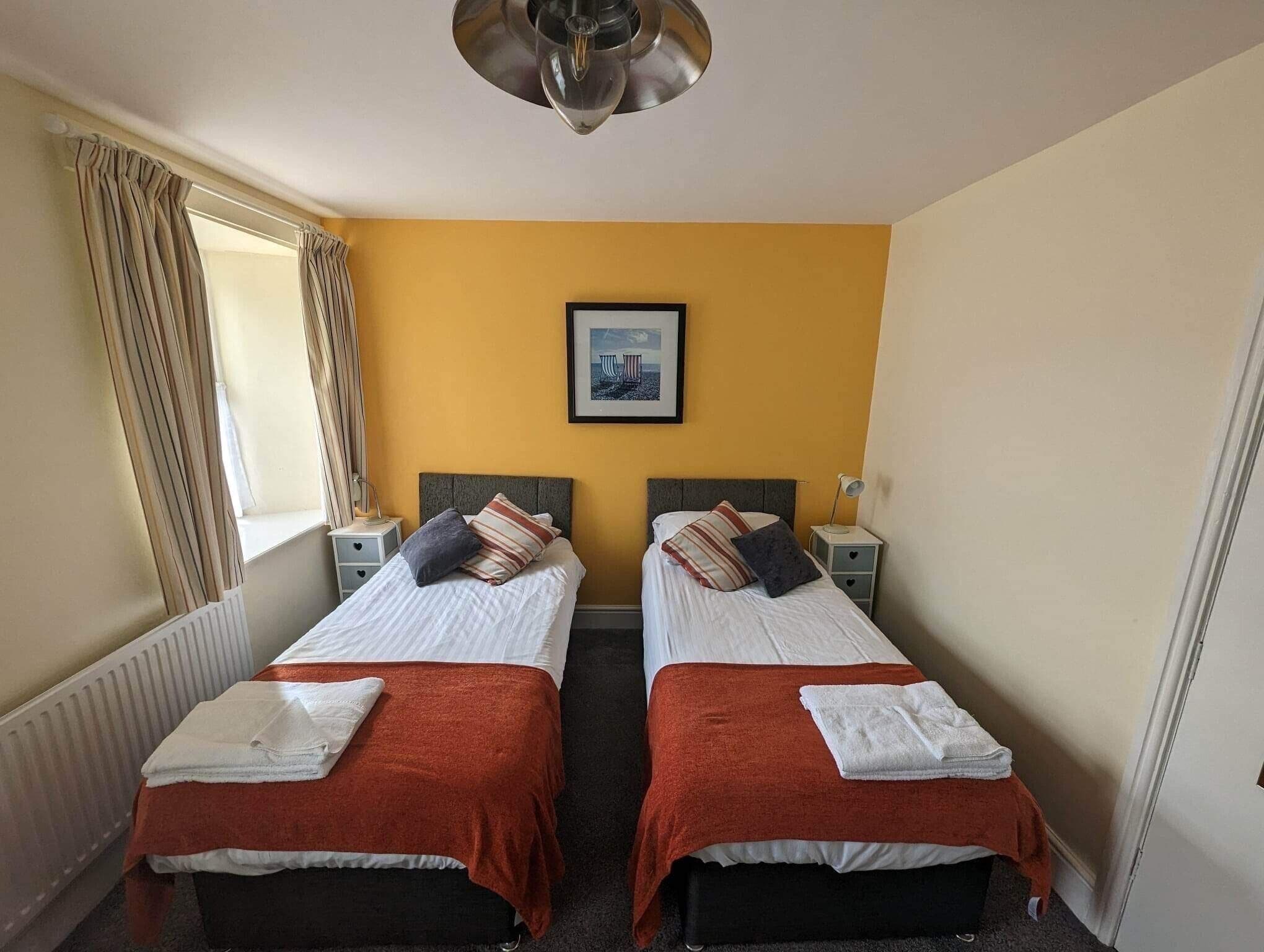 A hotel room with two beds, a framed picture on the wall, and a window with curtains.