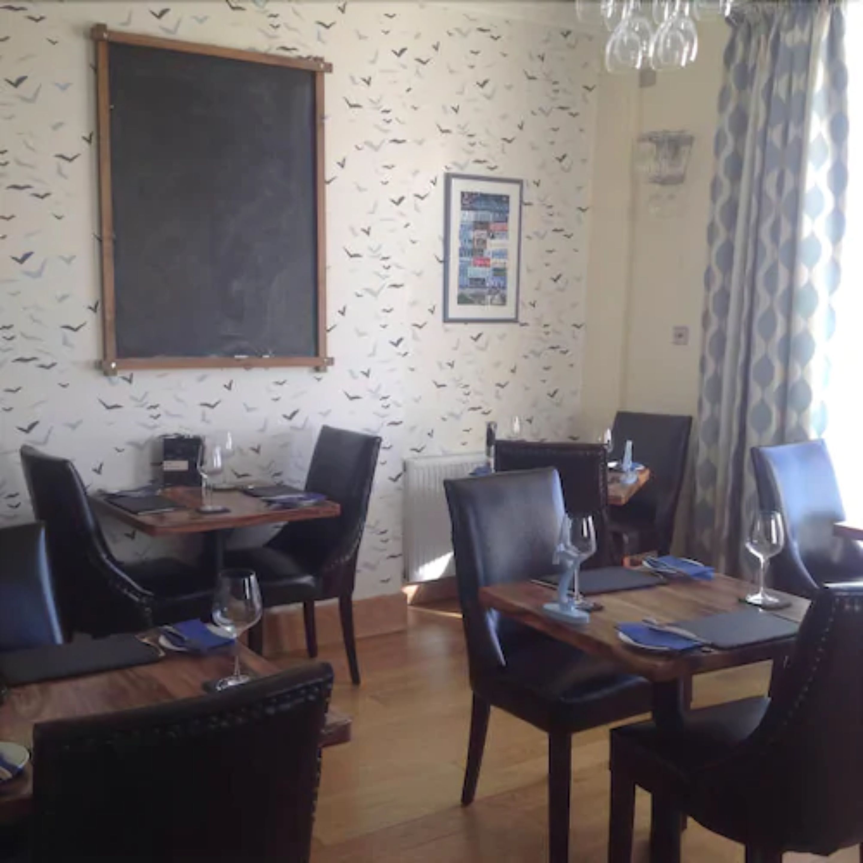A dining area with wooden tables and black chairs, a blackboard on the wall, and a framed picture.