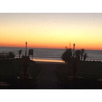 Vista del atardecer desde un paseo marítimo con farolas y palmeras.