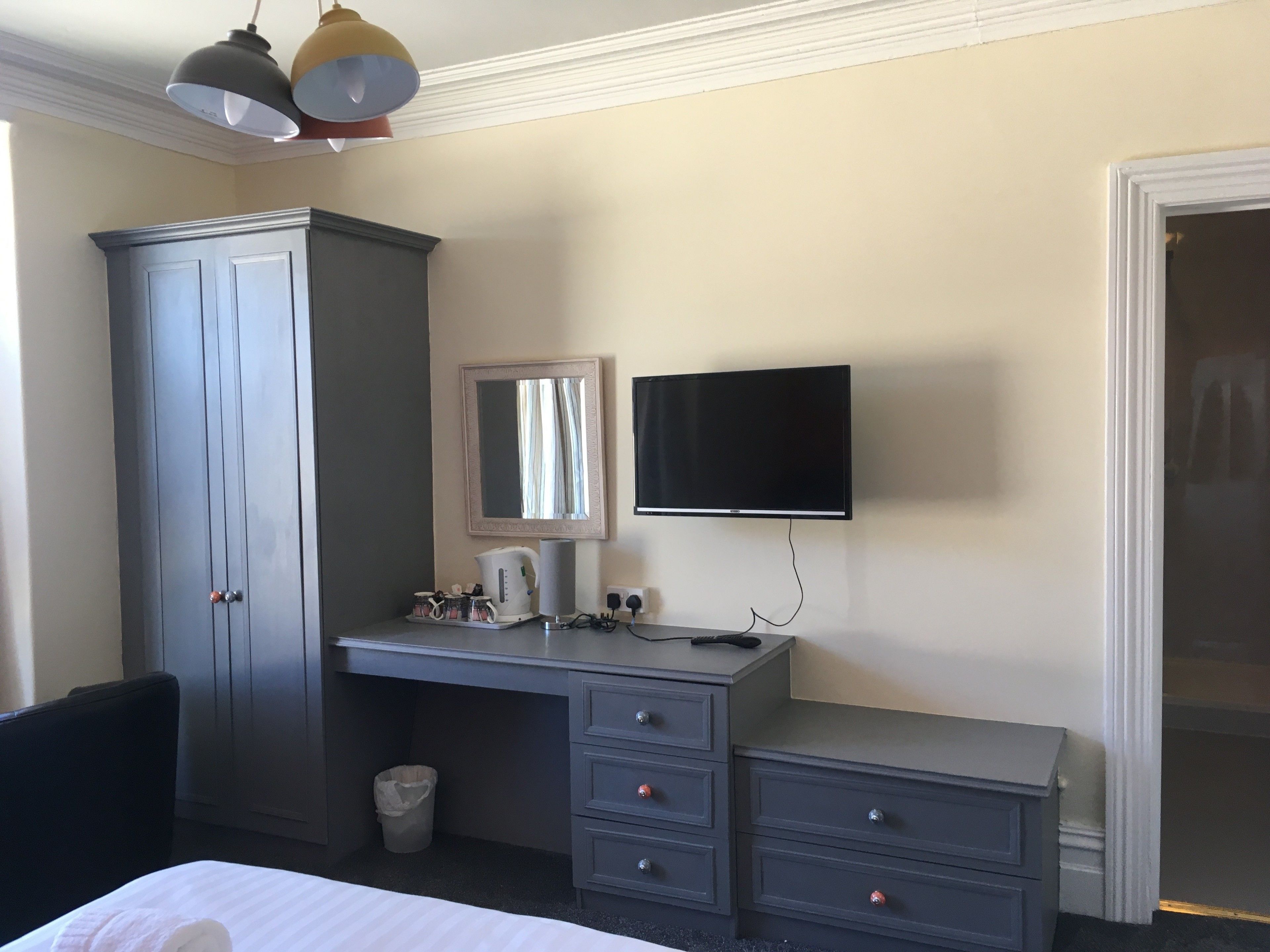 A hotel room with a bed, a desk with a chair, a wardrobe, a television, and a waste bin.