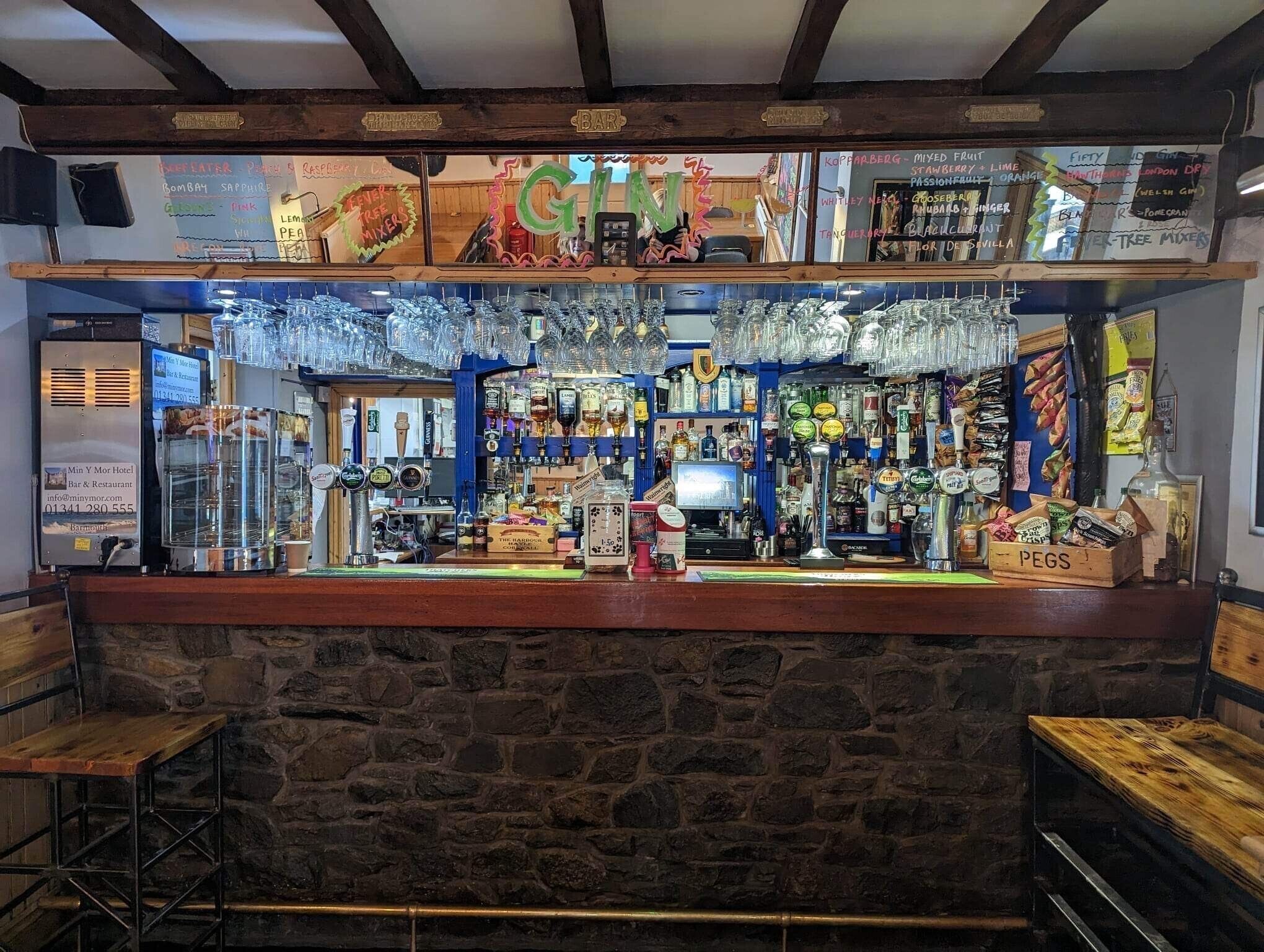 Zona de bar con pared de piedra, variedad de botellas de licor y un cartel que indica 'Bar'.