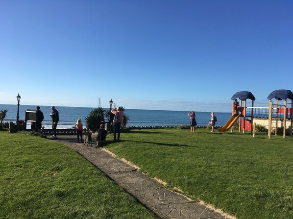 A park with a playground, a paved path, and a view of the sea.