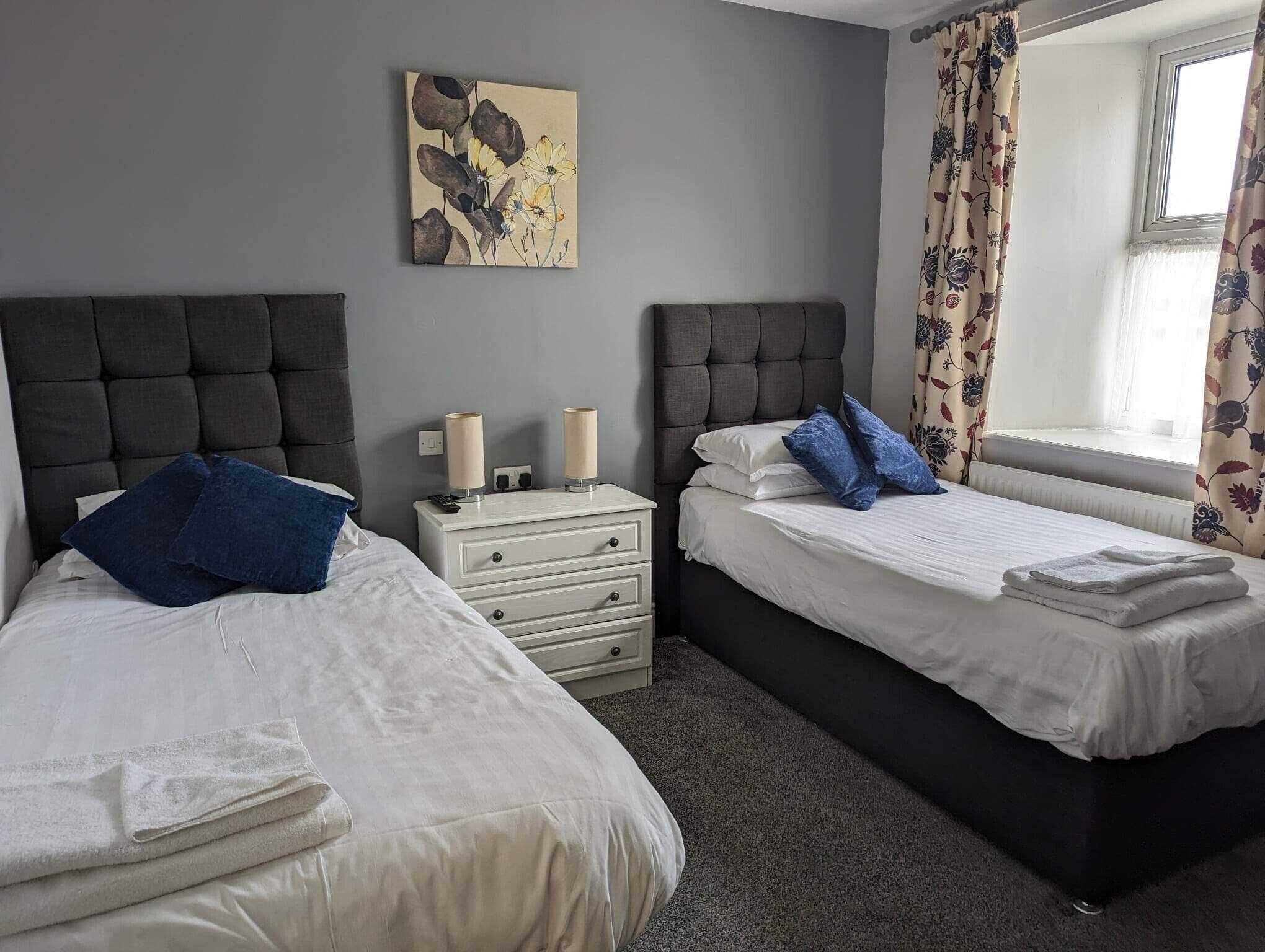 A bedroom with two beds, a nightstand, and a painting on the wall.