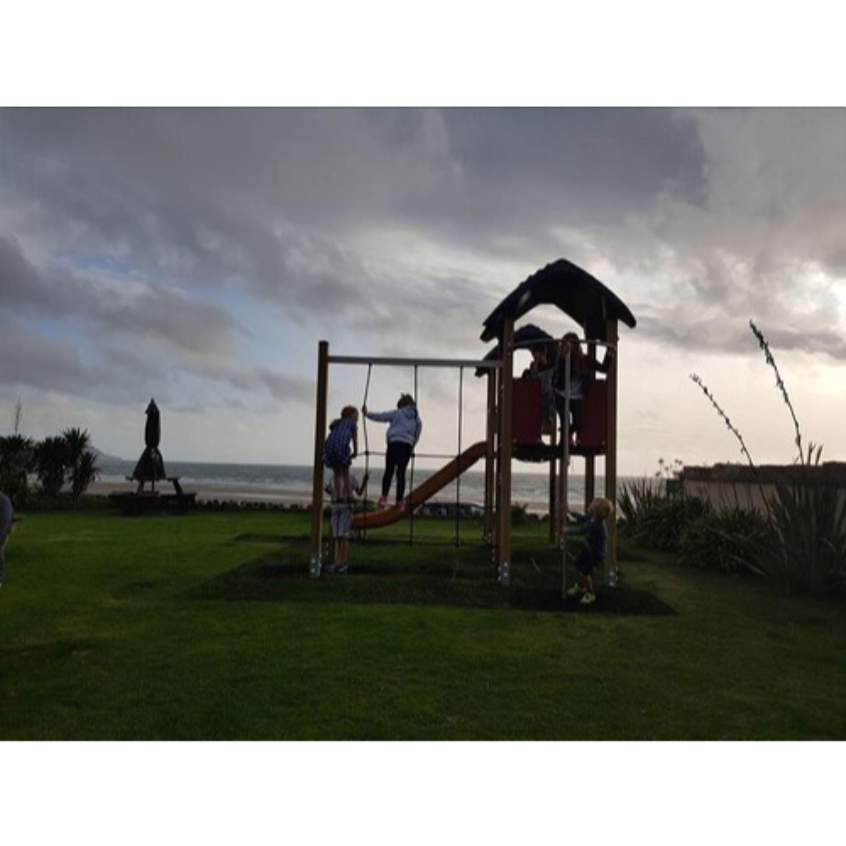 A playground with a slide and climbing structure in a grassy area with a view of the ocean.