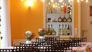 Un espace repas avec des tables préparées pour quatre personnes, un mur rempli de bouteilles de vin et une fenêtre avec des rideaux.