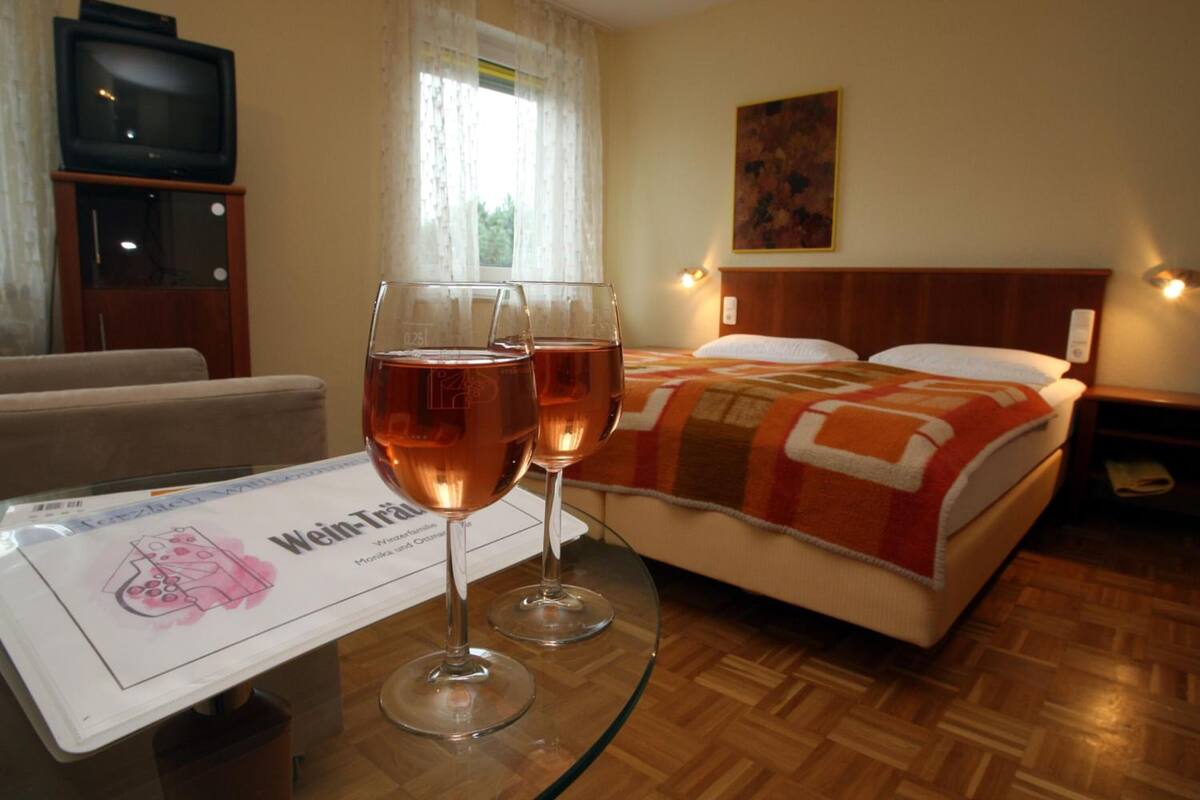 Une chambre d’hôtel avec un lit, une table en verre sur laquelle reposent deux verres à vin, un téléviseur et un tableau accroché au mur.