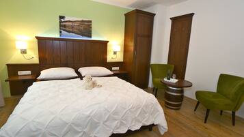 A hotel room with a large bed, two bedside lamps, a green chair, a wooden cabinet, and a small table with a bottle and glass.
