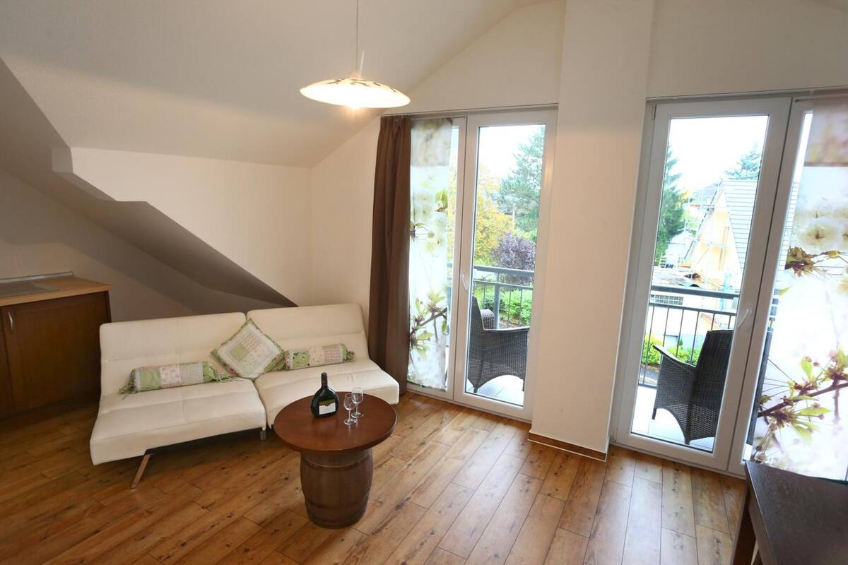 Une pièce avec un canapé blanc, une table basse en bois et une porte-fenêtre coulissante donnant sur un espace extérieur aménagé avec des chaises.
