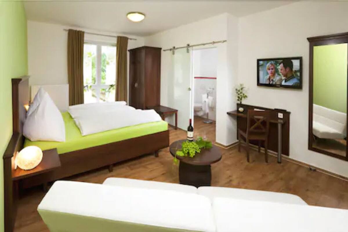 Une chambre d’hôtel avec un lit, un bureau, une chaise, un canapé, une télévision et une fenêtre.