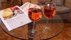 A hotel room with a bed, a sofa, and a glass table with two wine glasses and a magazine. - Hotel Wein-Träume (Thuengersheim)