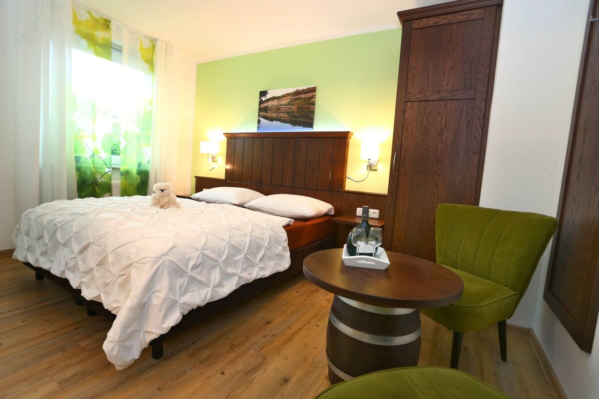 Une chambre d’hôtel avec un lit, une chaise verte, une table en bois et un tableau accroché au mur.