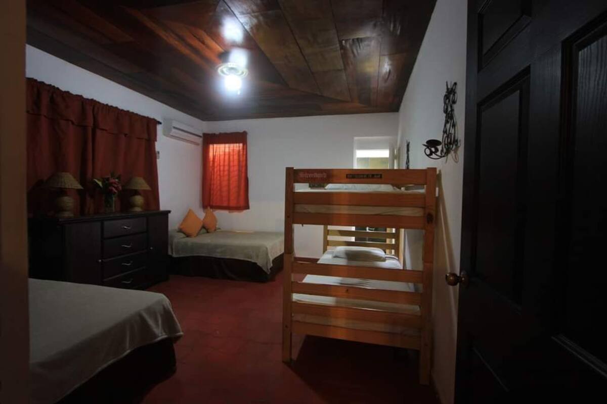 Une chambre avec un lit superposé, un lit simple, une commode et une porte.