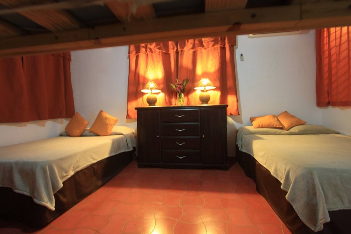 Une chambre avec deux lits, une commode et deux lampes.