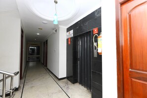 A hallway with a marble floor, a wooden door on the right, and a black door with a red "X" sign. - OYO 5208 The Park View Inn (Chennai)