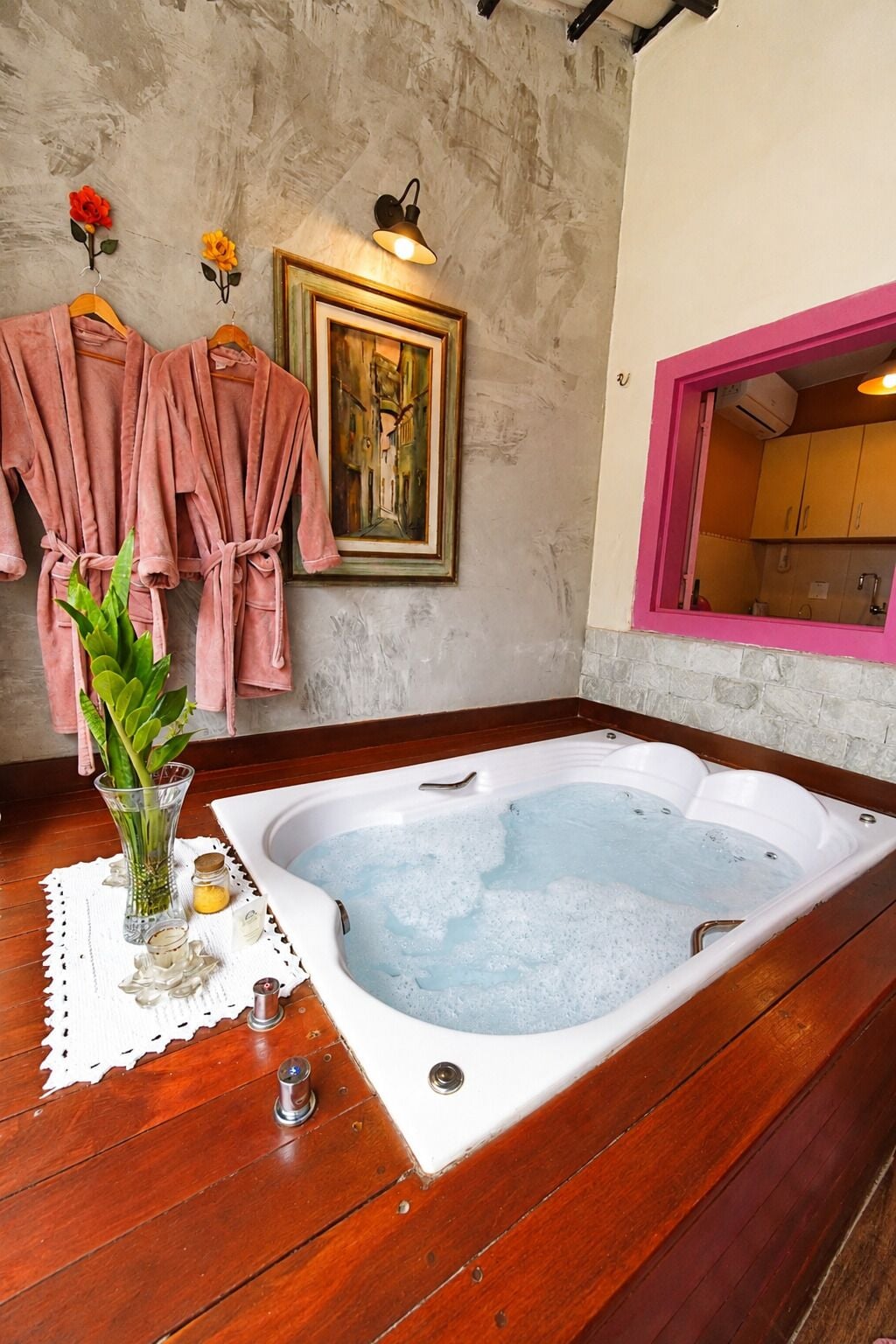 Een badkamer met een houten vloer, een badkuip, een ingelijst schilderij en roze handdoeken.
