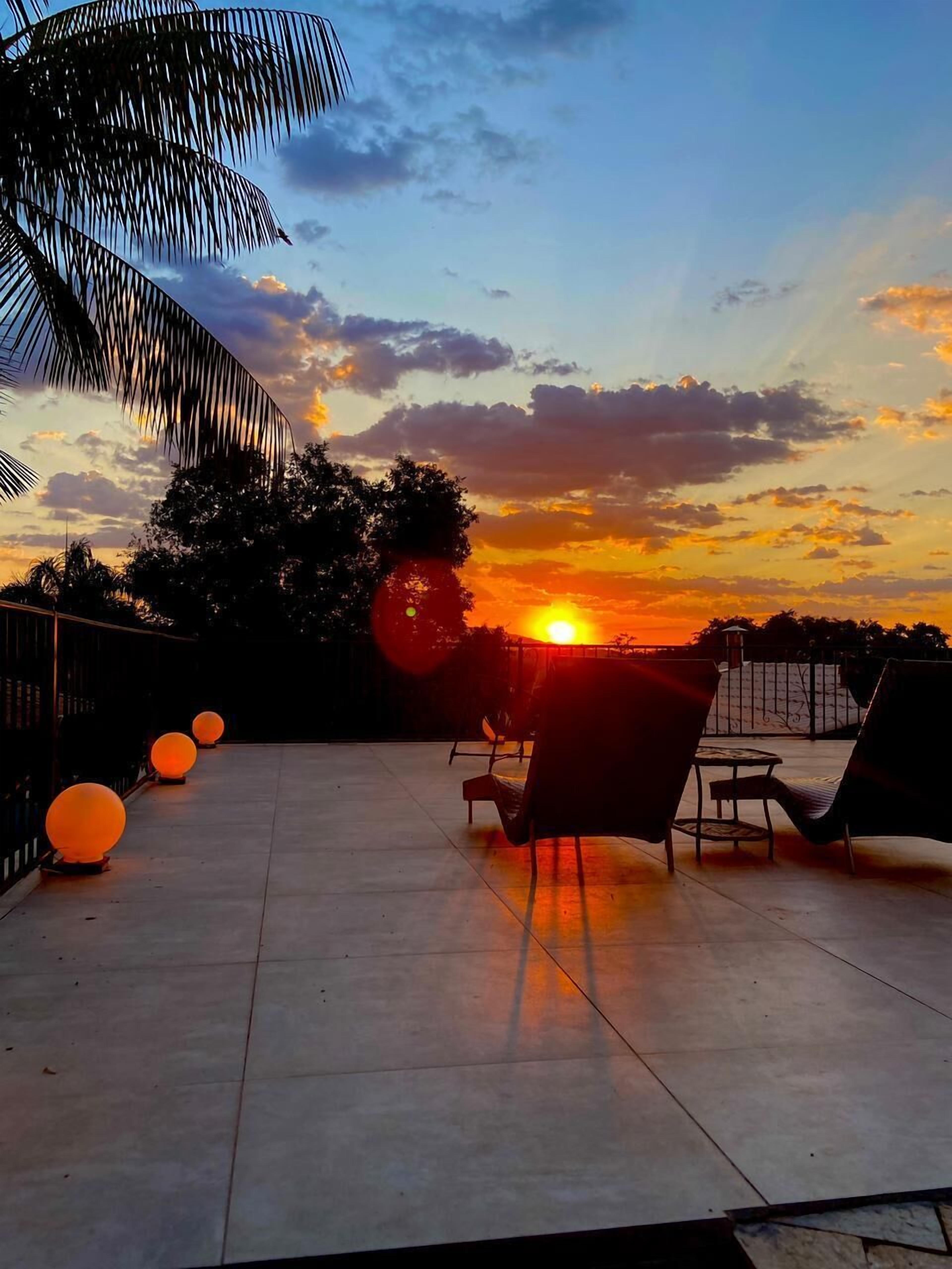 Een terras buiten met uitzicht op een zonsondergang, met een zithoek met stoelen en tafels, en decoratieve bolvormige lampen.