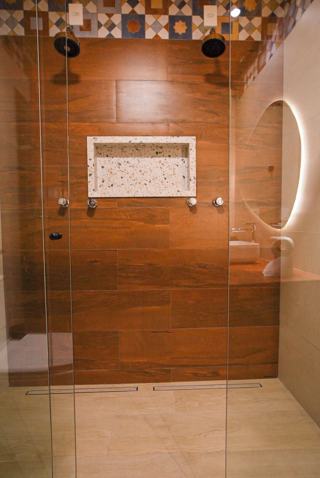 A modern shower with a wooden panel wall, a glass door, and a small shelf with a towel.