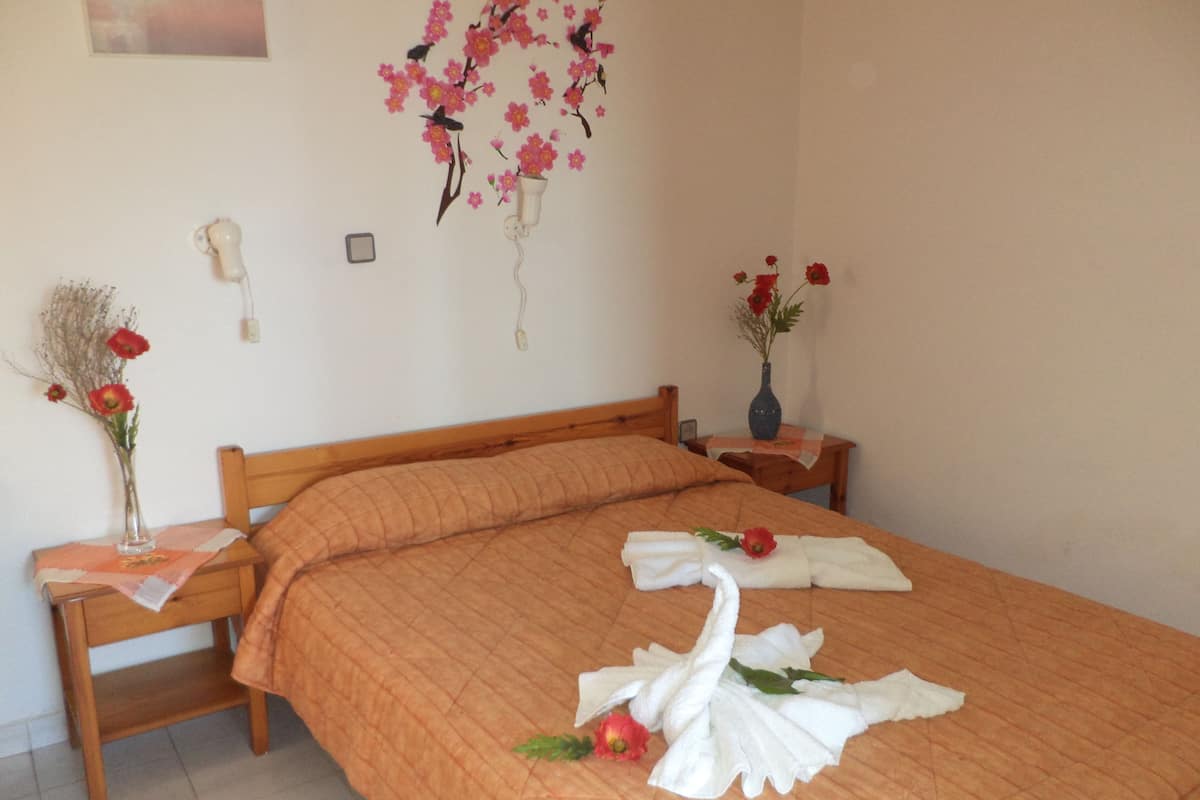 A neatly made bed with a swan towel arrangement, a vase with red flowers, and a wall decoration of pink flowers and birds.