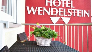 Une enseigne d'hôtel portant le nom « HÔTEL WENDELSTEIN » et un panier en osier rempli de fleurs, posé sur une table.