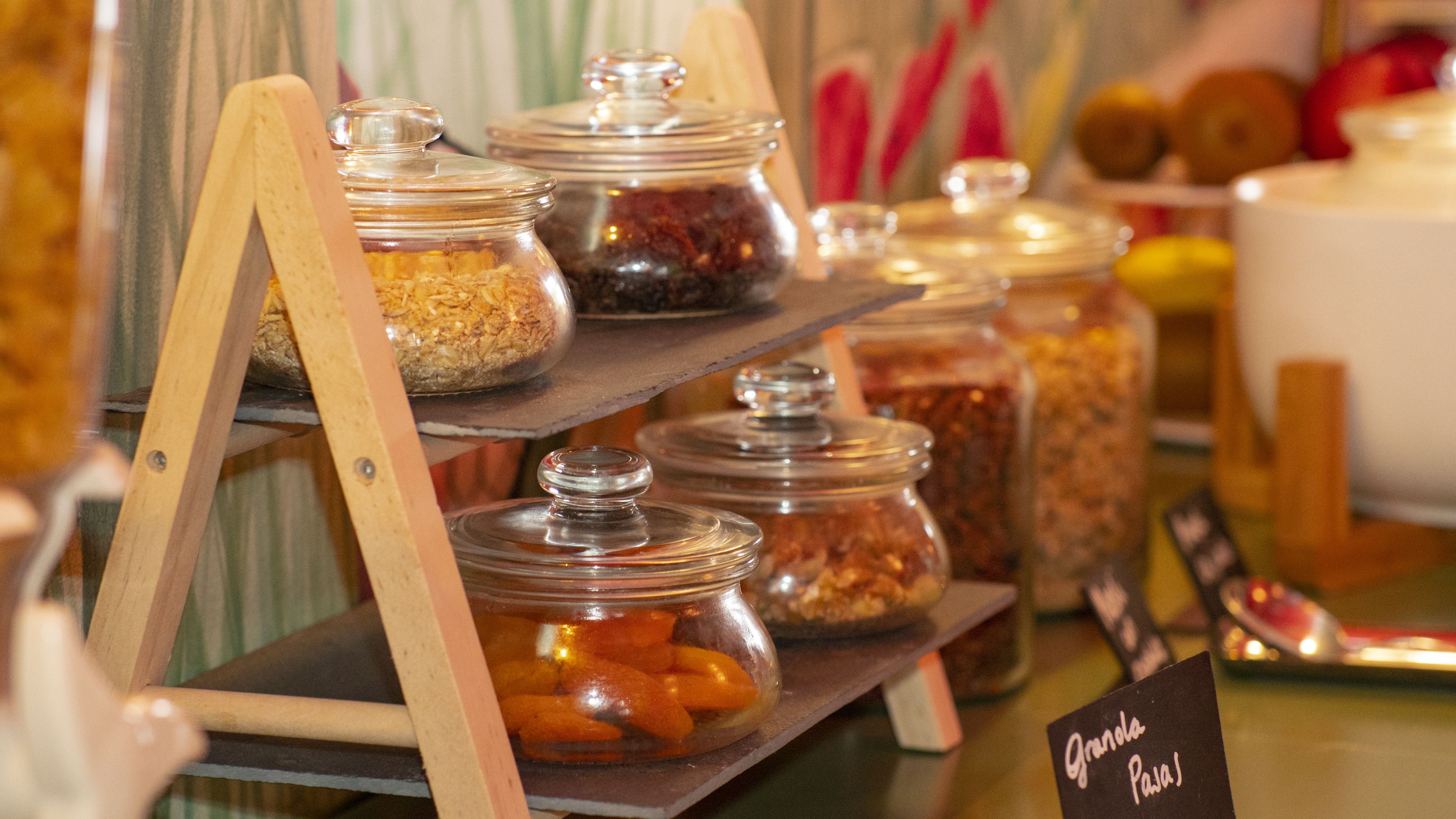 Una presentación de diferentes alimentos en frascos de vidrio sobre un soporte de madera.