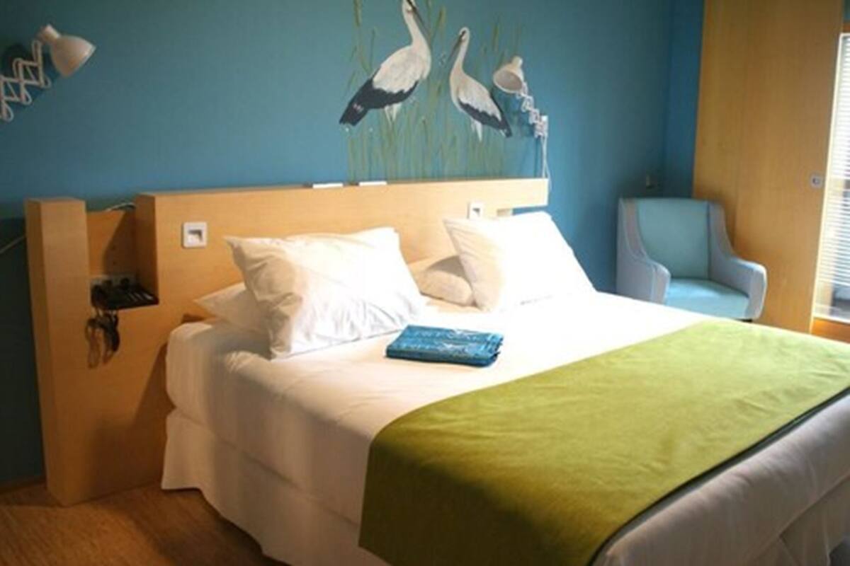 A hotel room with a bed, a chair, and a wall painting.