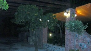 An outdoor area with a brick wall, a tree, and a covered seating area with lights. - Borgo Camicia In (Barcellona Pozzo di Gotto)