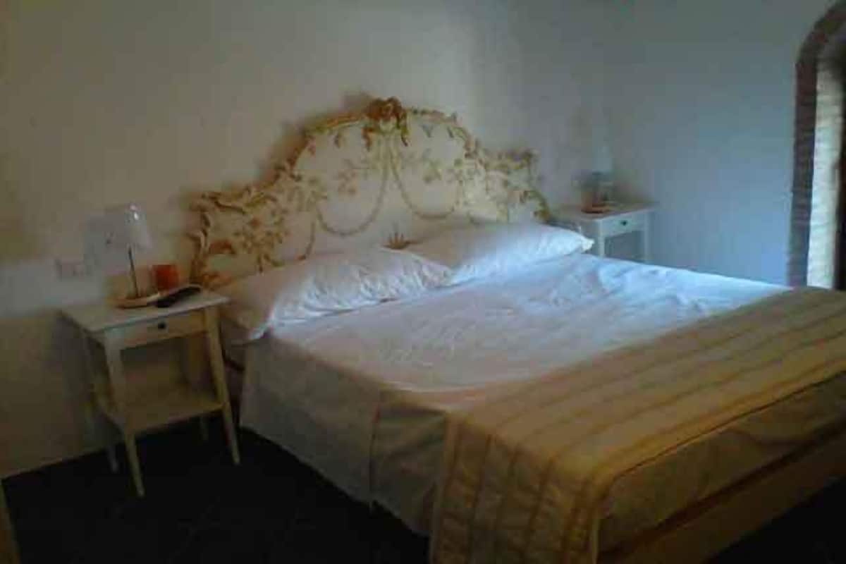 A single bed with a floral headboard, a bedside table with a lamp, and a nightstand with a phone.