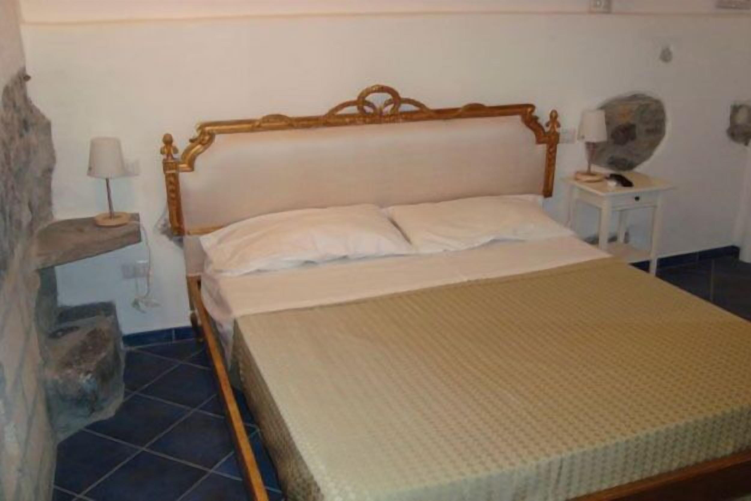 Um quarto com uma cama, uma mesa de cabeceira, uma luminária e uma parede de pedra.