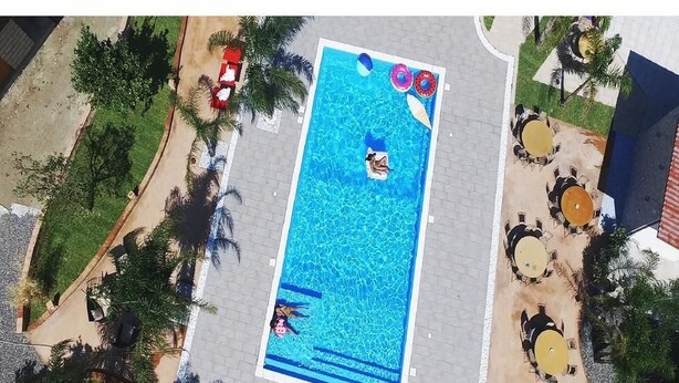 An aerial view of a rectangular swimming pool with two people in the water, surrounded by palm trees and outdoor seating areas. - Borgo Camicia In (Barcellona Pozzo di Gotto)