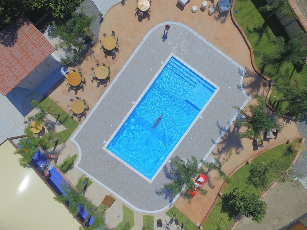 En vy från ovan av en swimmingpool omgiven av utomhusmöbler och grönska.