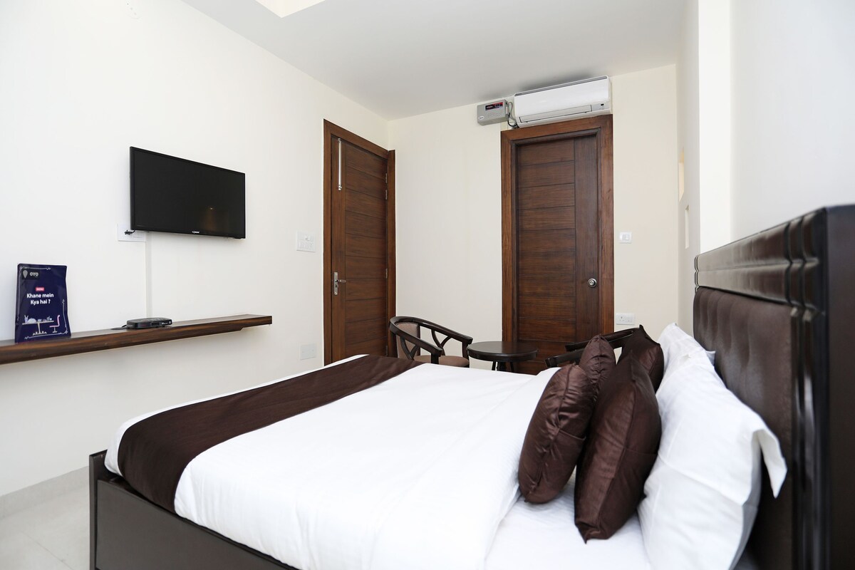 A hotel room with a bed, a TV mounted on the wall, a desk with a chair, and two doors.