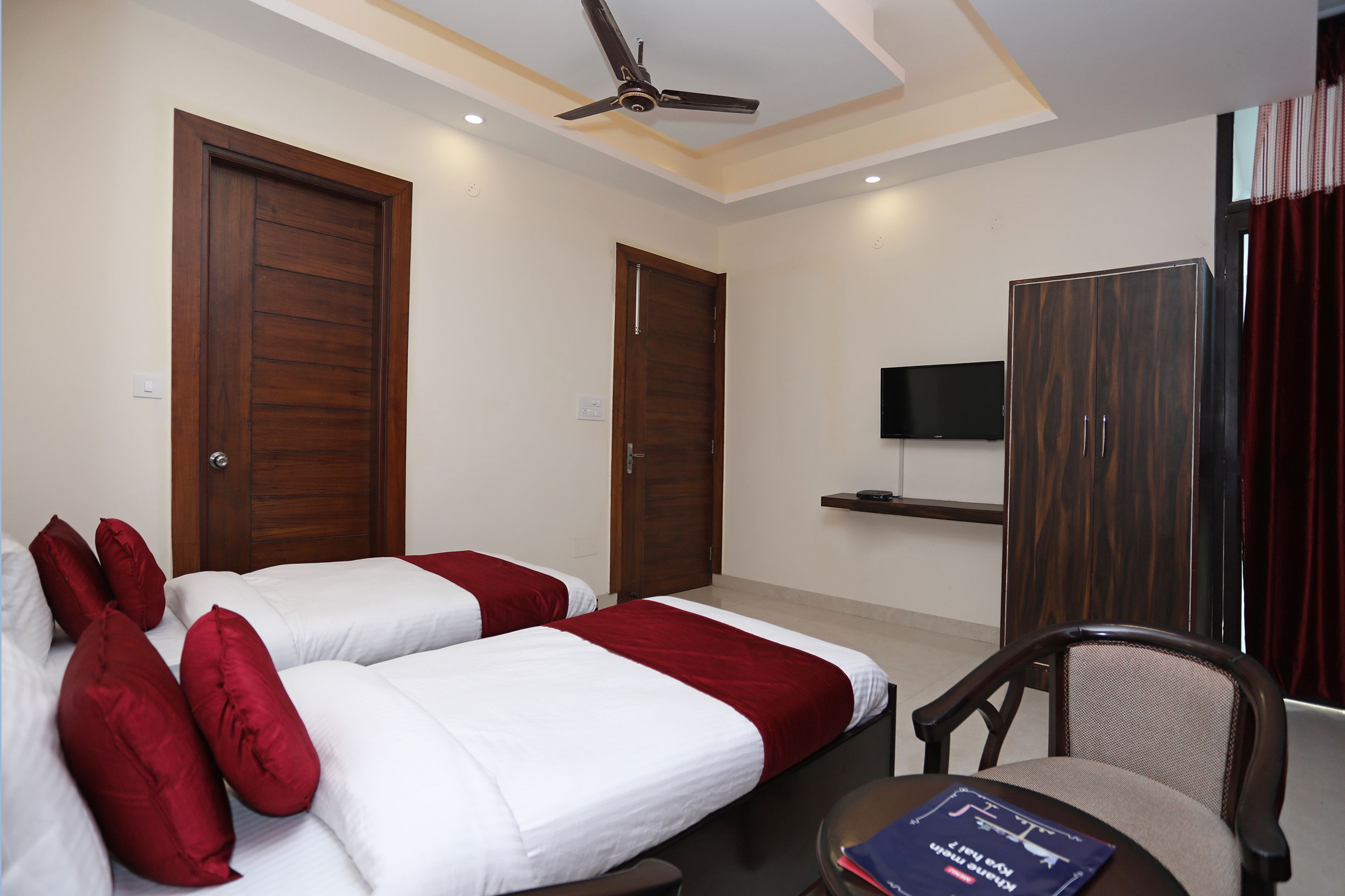 A hotel room with two beds, a ceiling fan, a TV, and a wooden wardrobe.