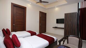 A hotel room with two beds, a ceiling fan, a TV, and a wooden wardrobe.