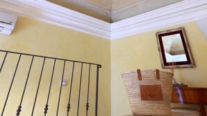 Una habitación con un techo decorativo, barandal de metal, cesta tejida y un cuadro en la pared.