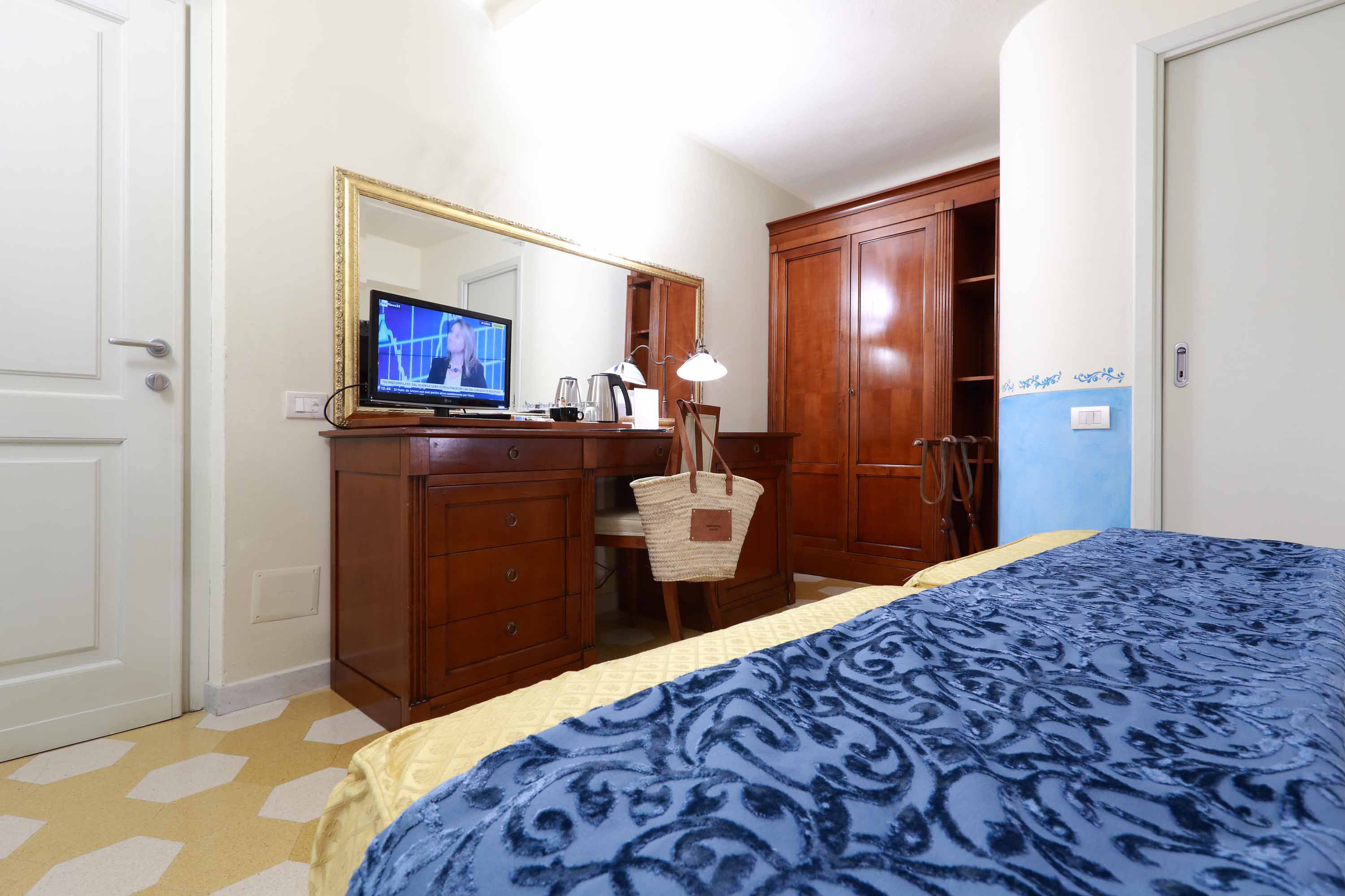 A bedroom with a bed, a desk with a computer, a chair, a lamp, and a wardrobe.