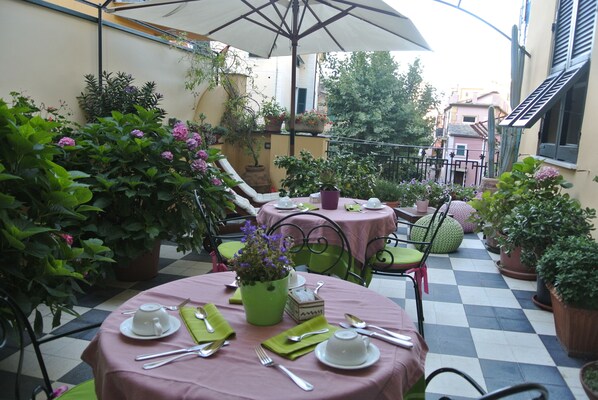 A terrace with round tables, chairs, and potted plants. - Locanda Il Maestrale (Monterosso al Mare)