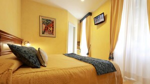 Una habitación de hotel con una cama, un cuadro en la pared, un televisor y una ventana con cortinas.