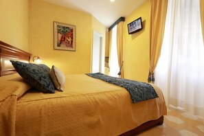 A hotel room with a bed, a painting on the wall, a television, and a window with curtains. - Locanda Il Maestrale (Monterosso al Mare)
