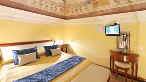 Habitación de hotel con cama, escritorio con silla, televisión y espejo.