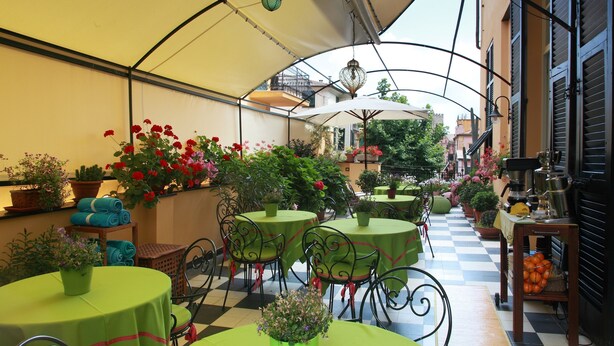 Un café al aire libre con mesas y sillas, plantas en macetas y un suelo de cuadros.