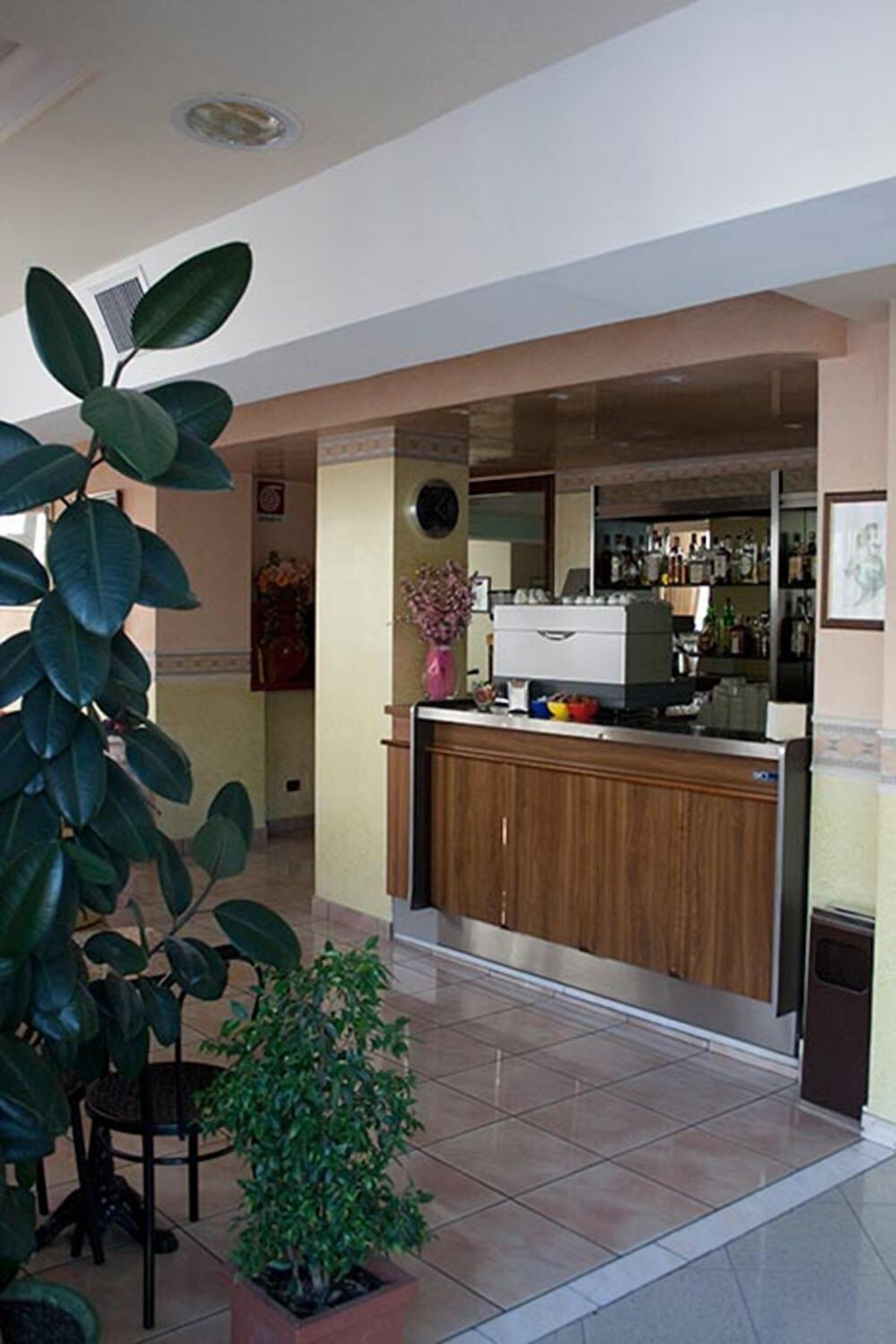 A kitchen area with a wooden counter, a sink, and a refrigerator. There are potted plants and a vase with flowers on the counter.