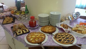 Una mesa de buffet con diferentes opciones de comida, incluyendo tartas, pasteles y una botella de bebida roja.