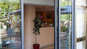 Un vestíbulo de hotel con mostrador de recepción, una planta en maceta y una entrada de vidrio.