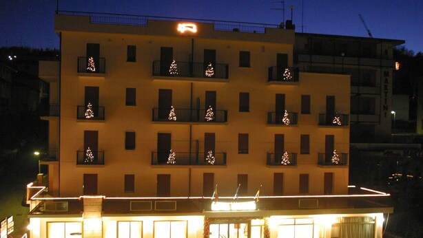 Un hotel de varios pisos con balcones, un área de restaurante en la planta baja y una entrada visible.