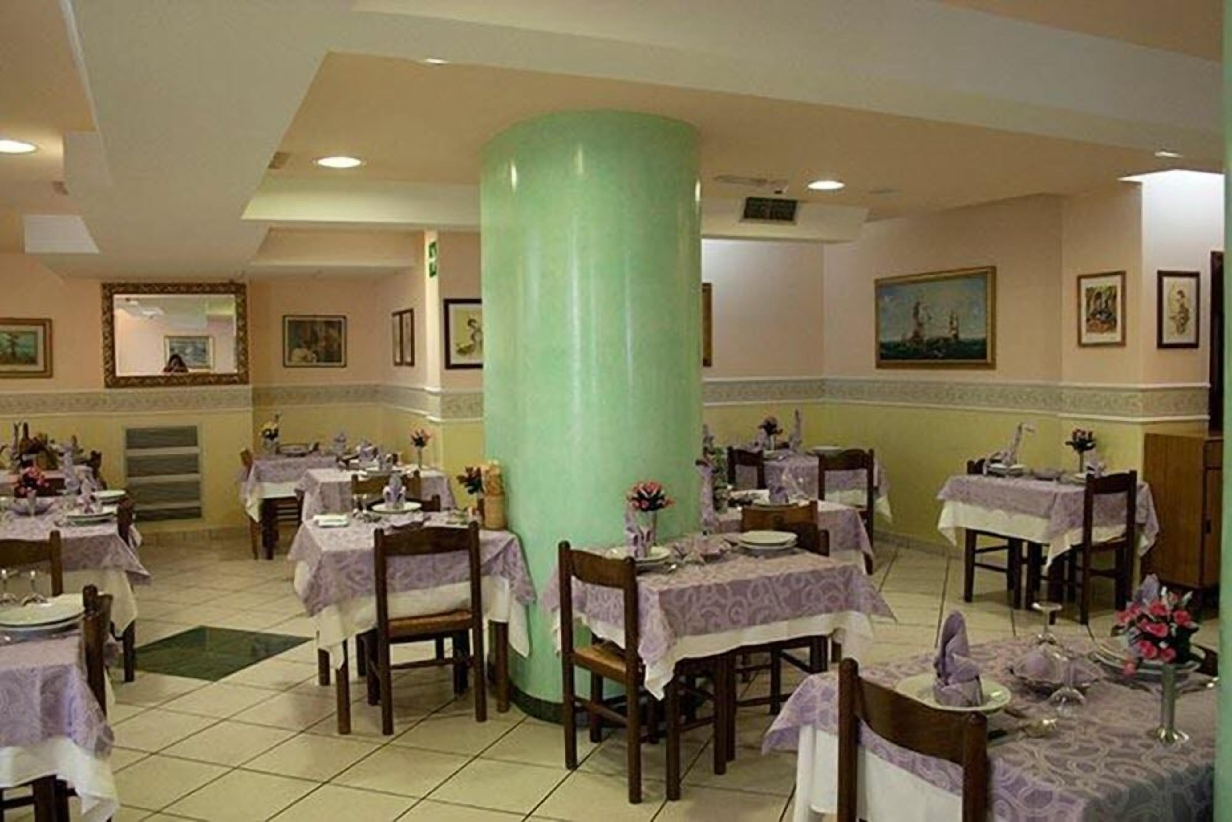 A dining area with tables set for multiple guests, a large green pillar, and framed artwork on the walls.
