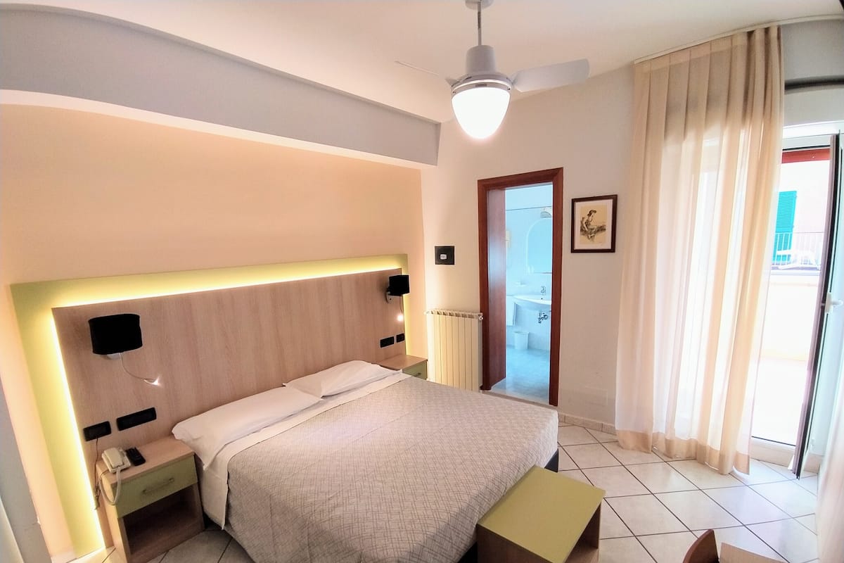 Una habitación de hotel con cama, mesita de noche y un pequeño escritorio con una silla.
