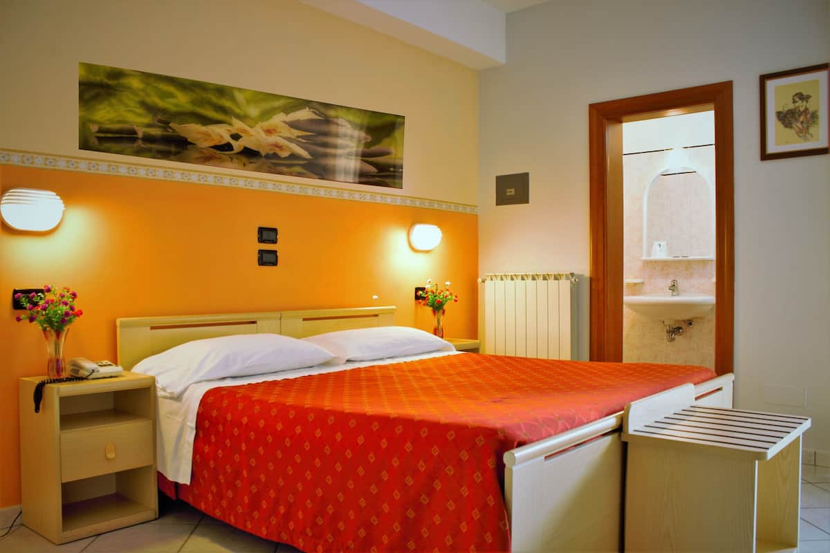 Una habitación de hotel con cama, mesita de noche y un cuadro en la pared.